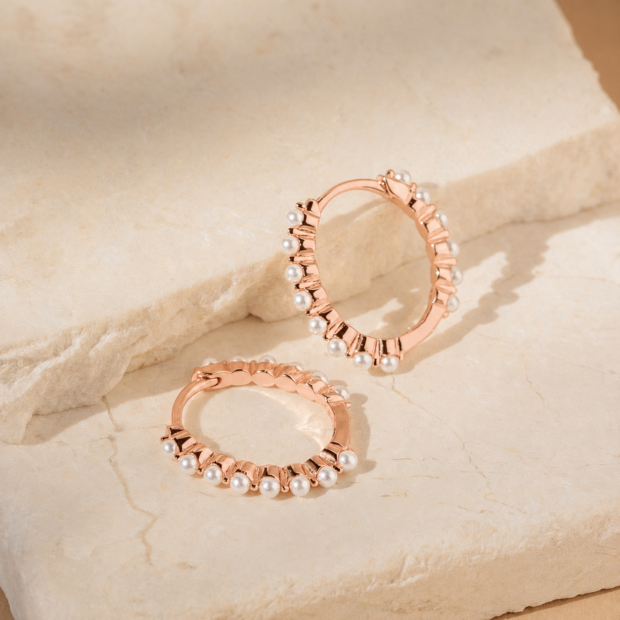 Rose gold hoop earrings with pearls on a beige stone surface
