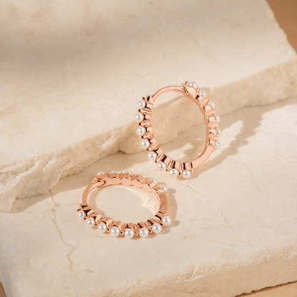 Rose gold hoop earrings with pearls on a beige stone surface