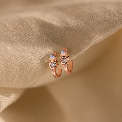 Rose gold hoop earrings with gemstones on a beige fabric background