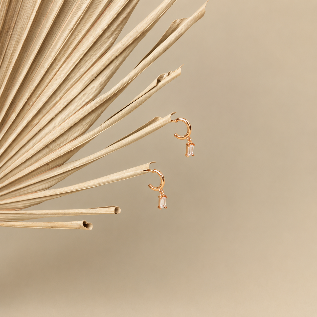 Gold earrings with pink gemstones on a beige background