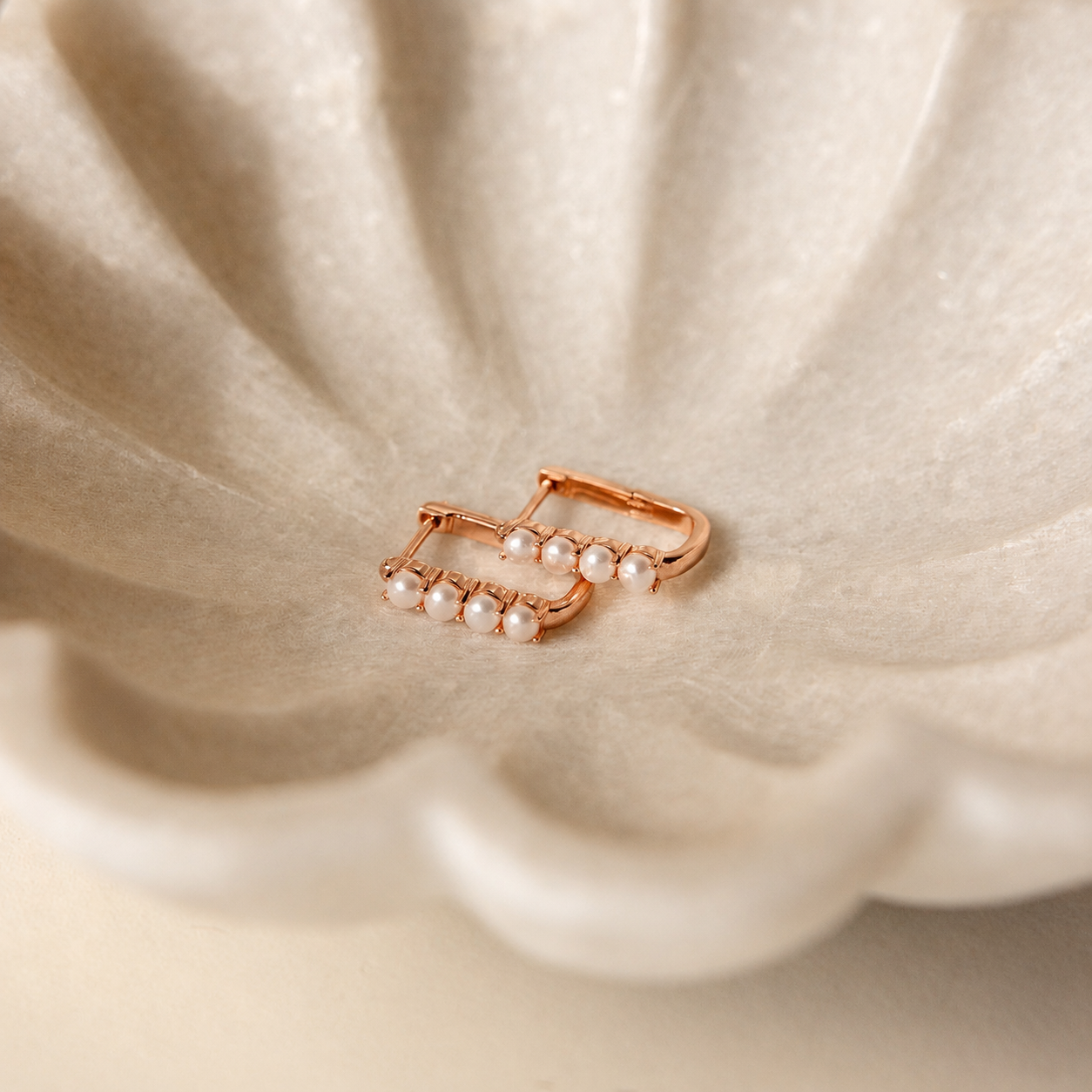Rose gold earring with pearls on a beige fabric background