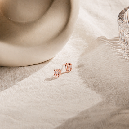 Rose gold stud earrings on a textured beige surface