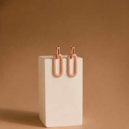 Rose gold earrings on a white stand against a brown background