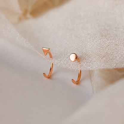Two rose gold earrings on a soft beige fabric background