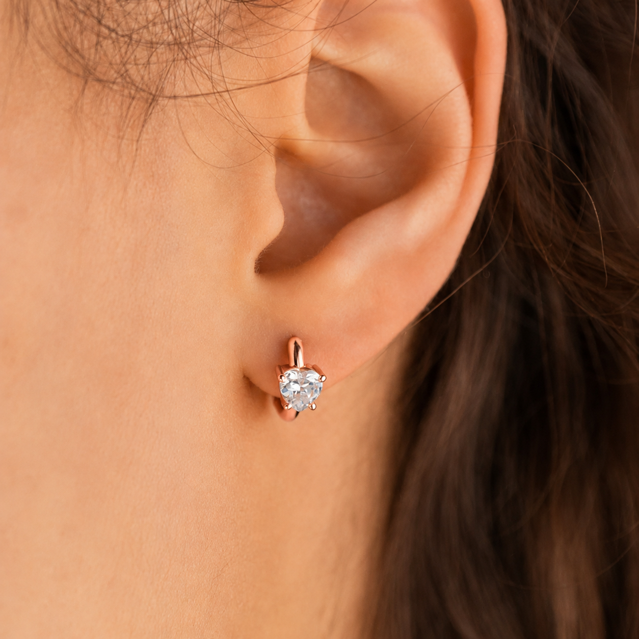 Close-up of an ear wearing a rose gold earring with a clear gemstone.