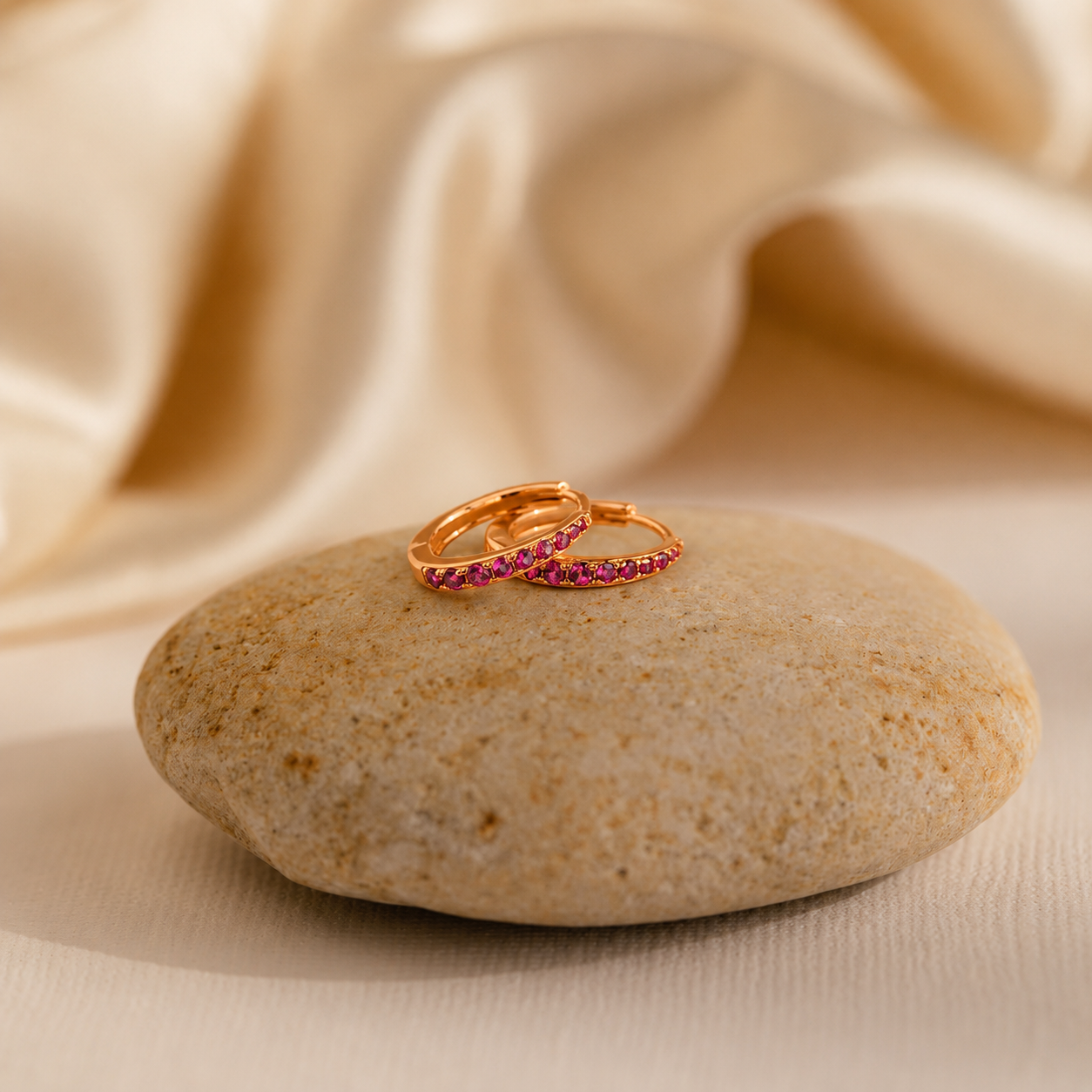 Two gold rings with red gemstones on a stone with beige fabric background