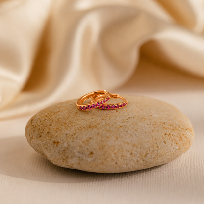 Two gold rings with red gemstones on a stone with beige fabric background