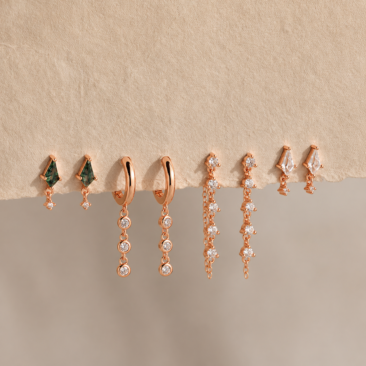 Set of rose gold earrings on a beige surface