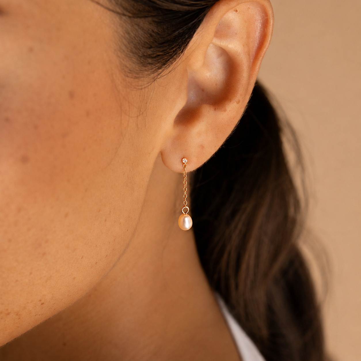 Close-up of an ear wearing a gold earring with a pearl drop against a neutral background