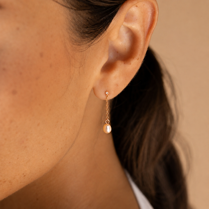 Close-up of an ear wearing a gold earring with a pearl drop against a neutral background