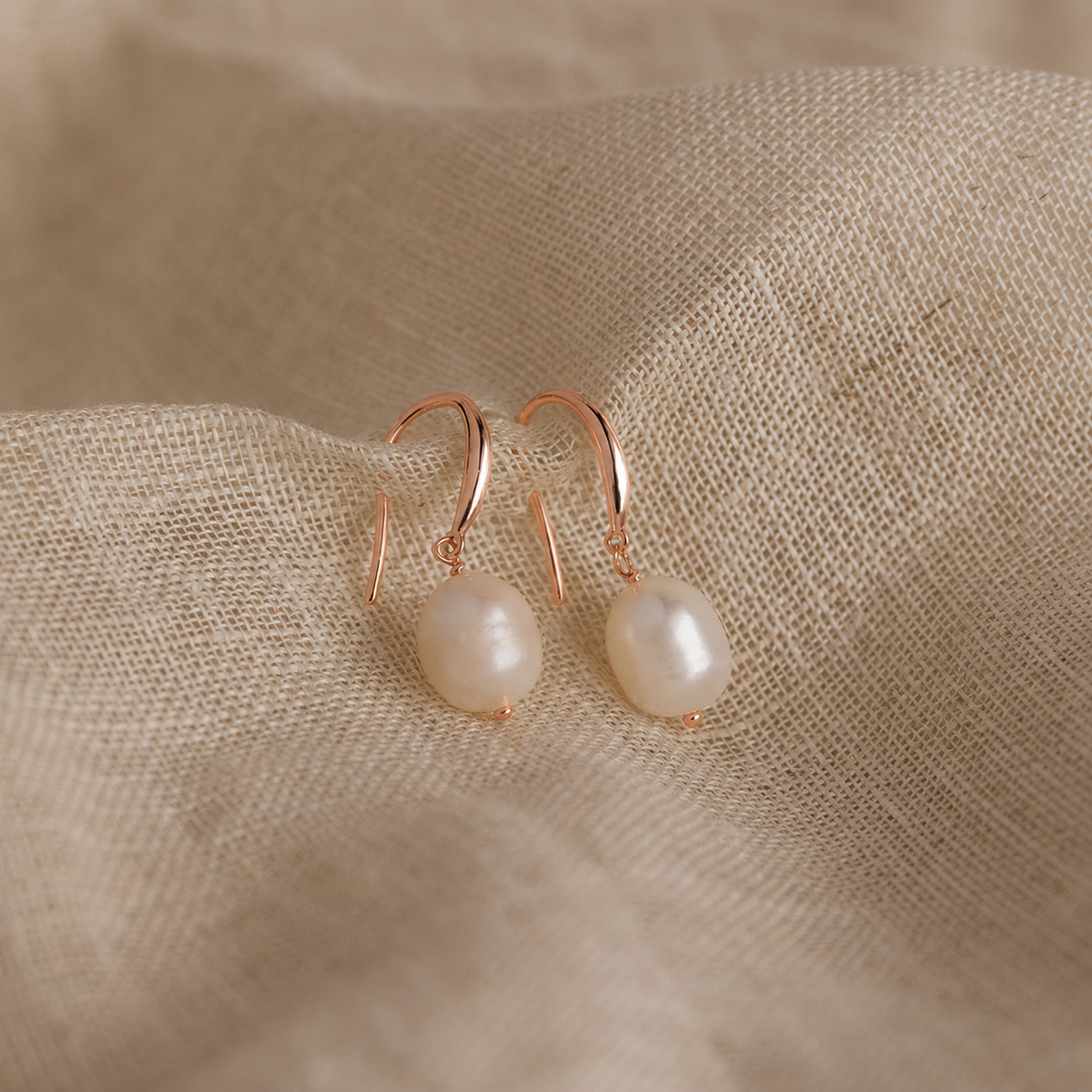 Pair of pearl earrings with rose gold hooks on a beige fabric background