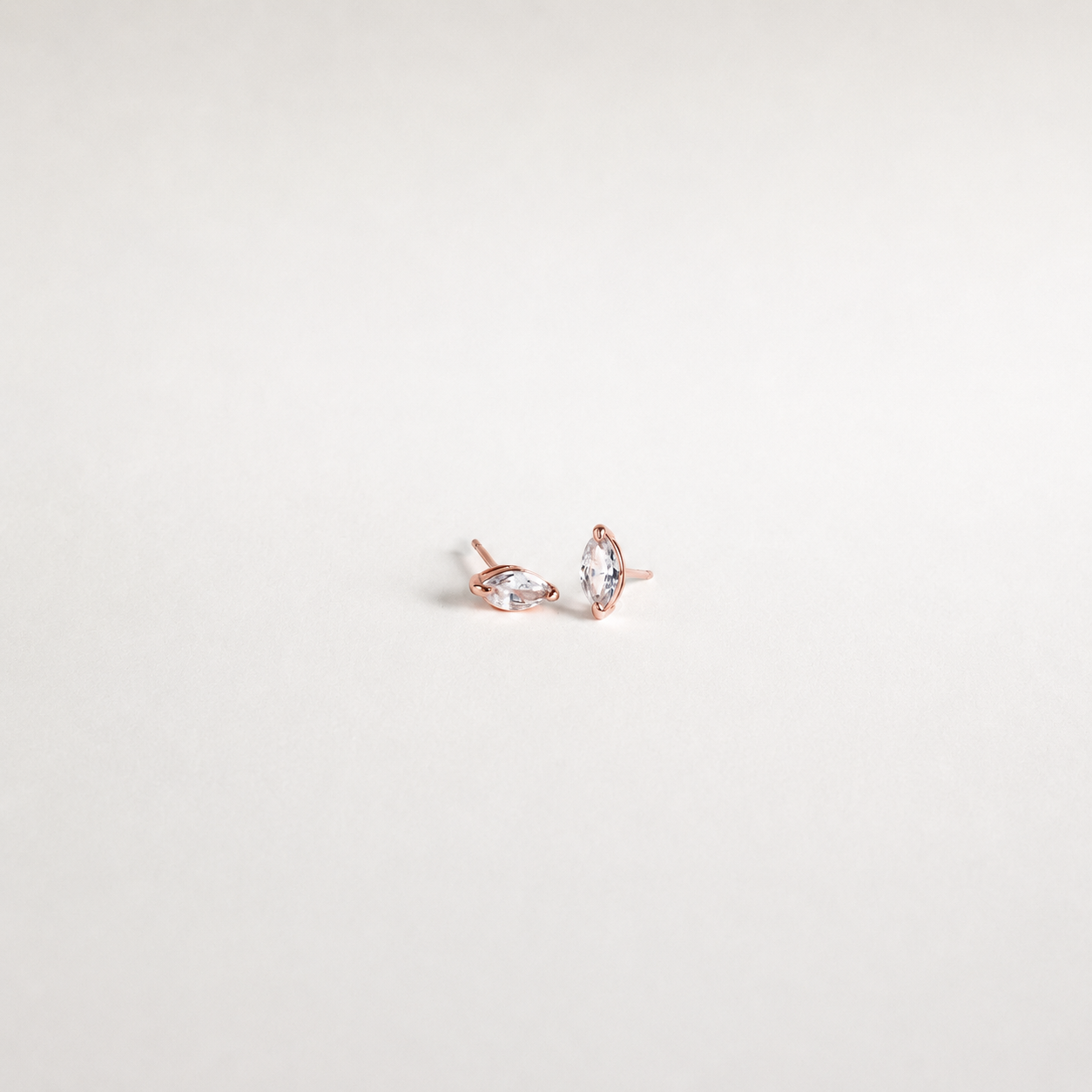 A pair of rose gold stud earrings with marquise-cut clear gemstones, displayed on a clean, light off-white background.