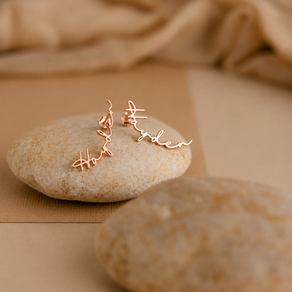 Rose gold earrings with 'love' and 'mother' inscriptions on a stone surface.