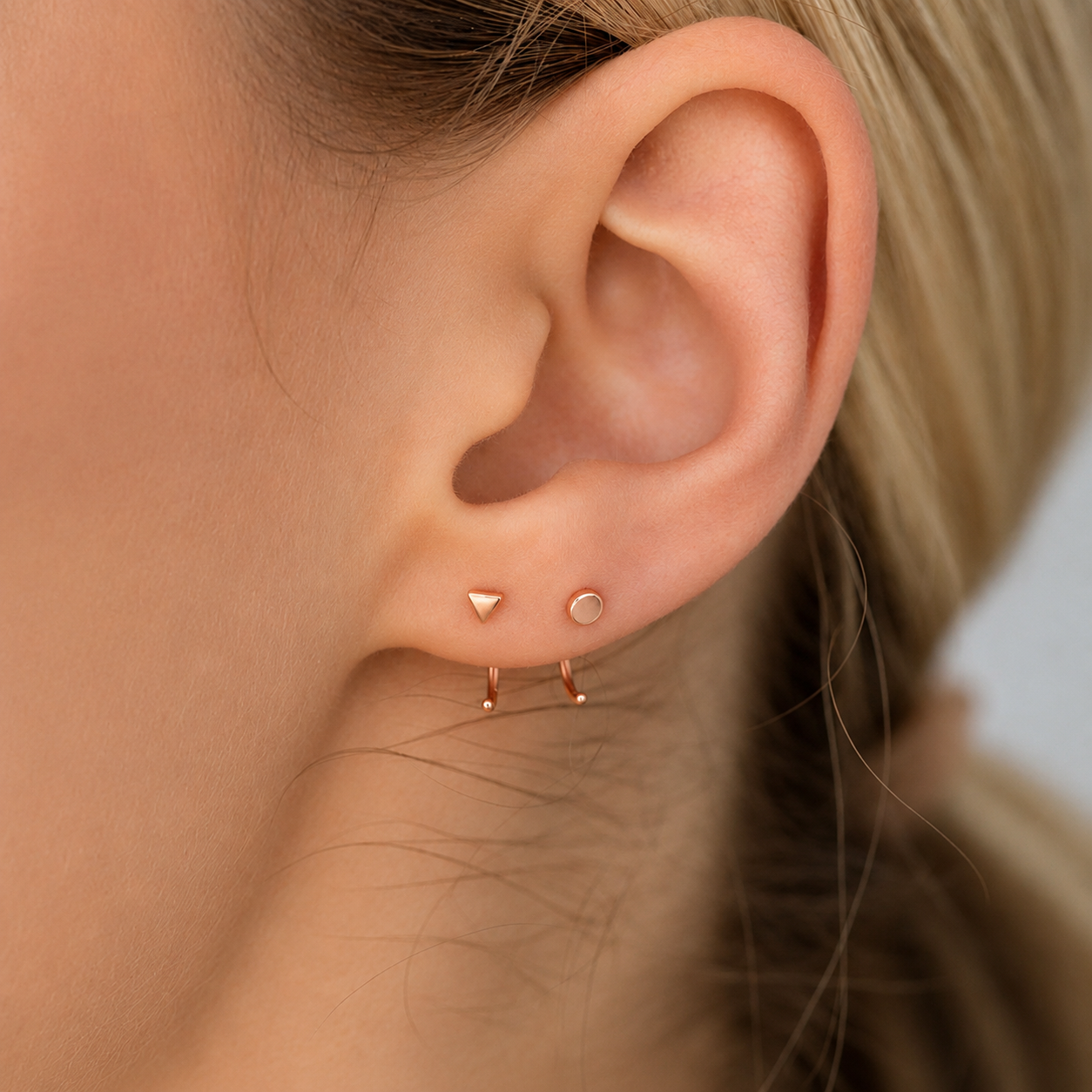 Close-up of an ear wearing three gold earrings against a neutral background