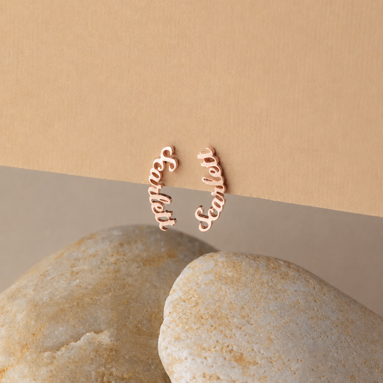 Rose gold earrings with 'Sister' and 'Bella' text on a beige background