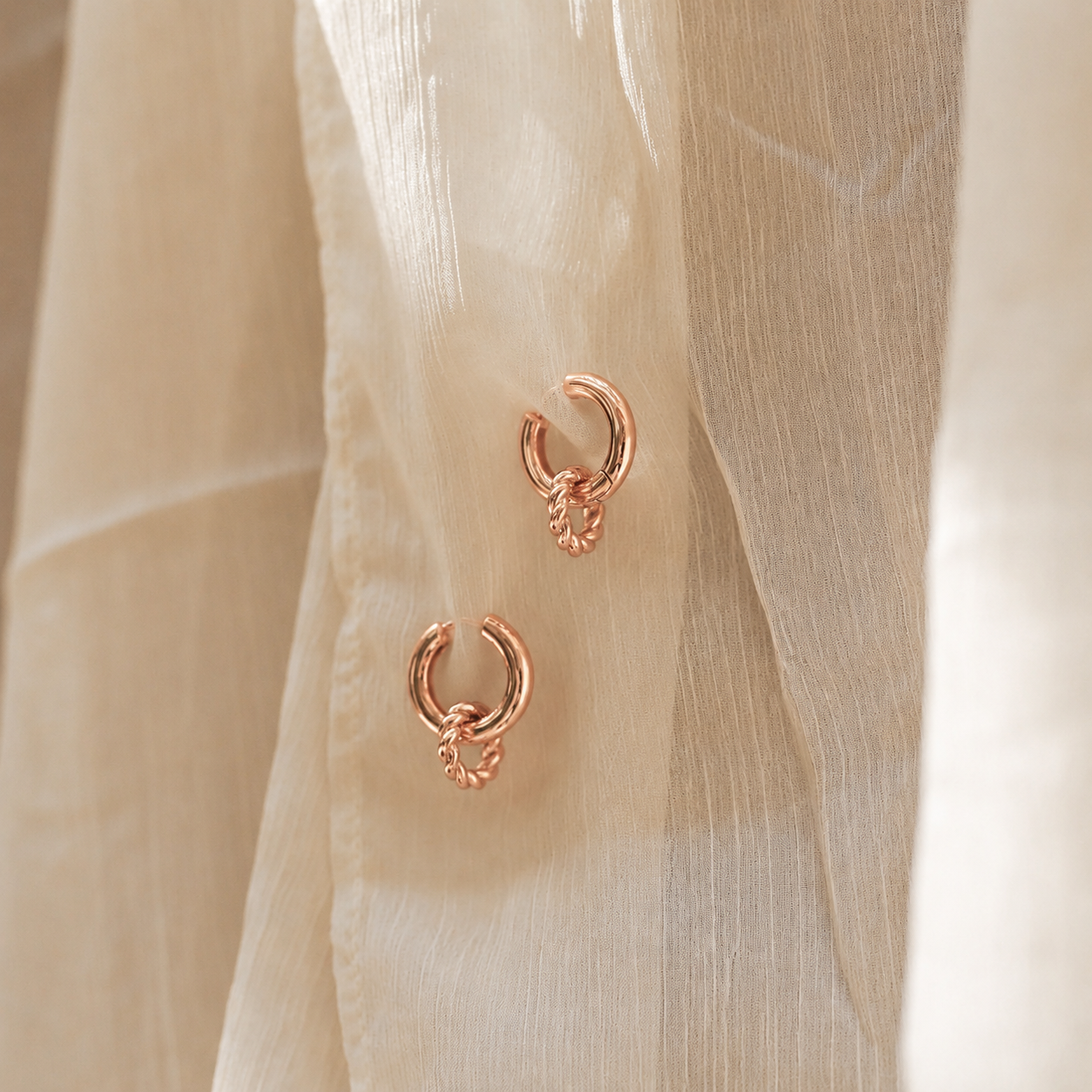 Rose gold hoop earrings on a beige fabric background