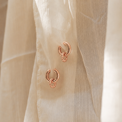 Rose gold hoop earrings on a beige fabric background