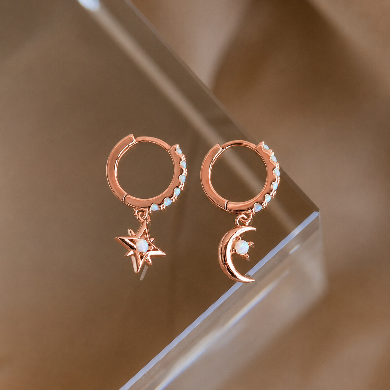 Rose gold hoop earrings with star and moon charms on a reflective surface.