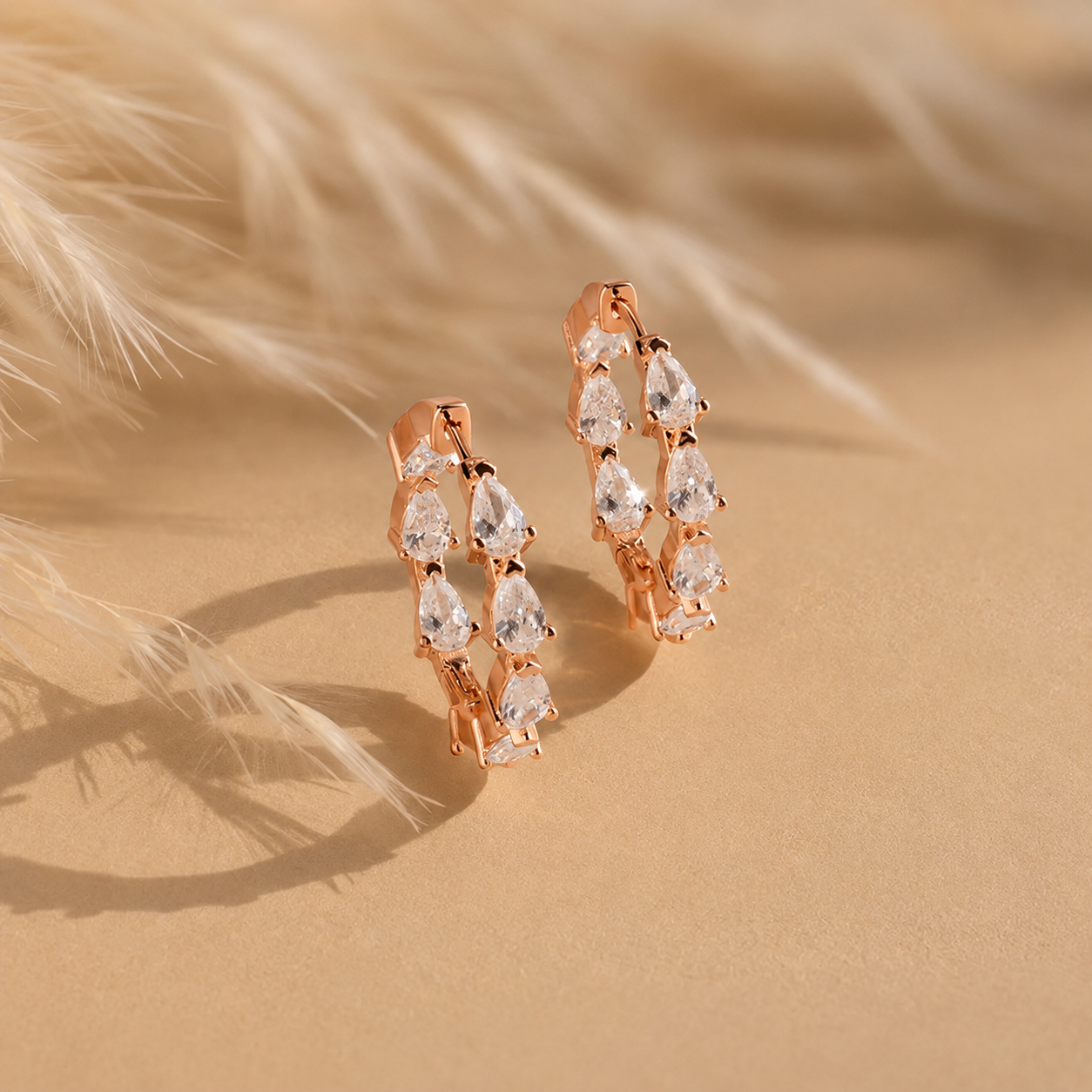 Rose gold hoop earrings with clear gemstones on a sandy background