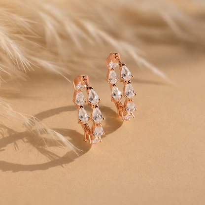 Rose gold hoop earrings with clear gemstones on a sandy background