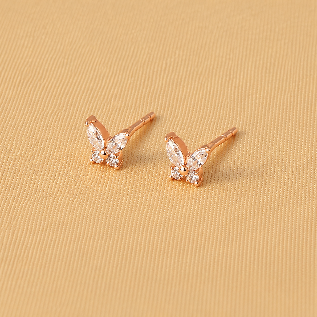 Rose gold butterfly earrings with clear gemstones on a beige fabric background