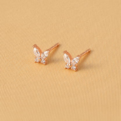 Rose gold butterfly earrings with clear gemstones on a beige fabric background