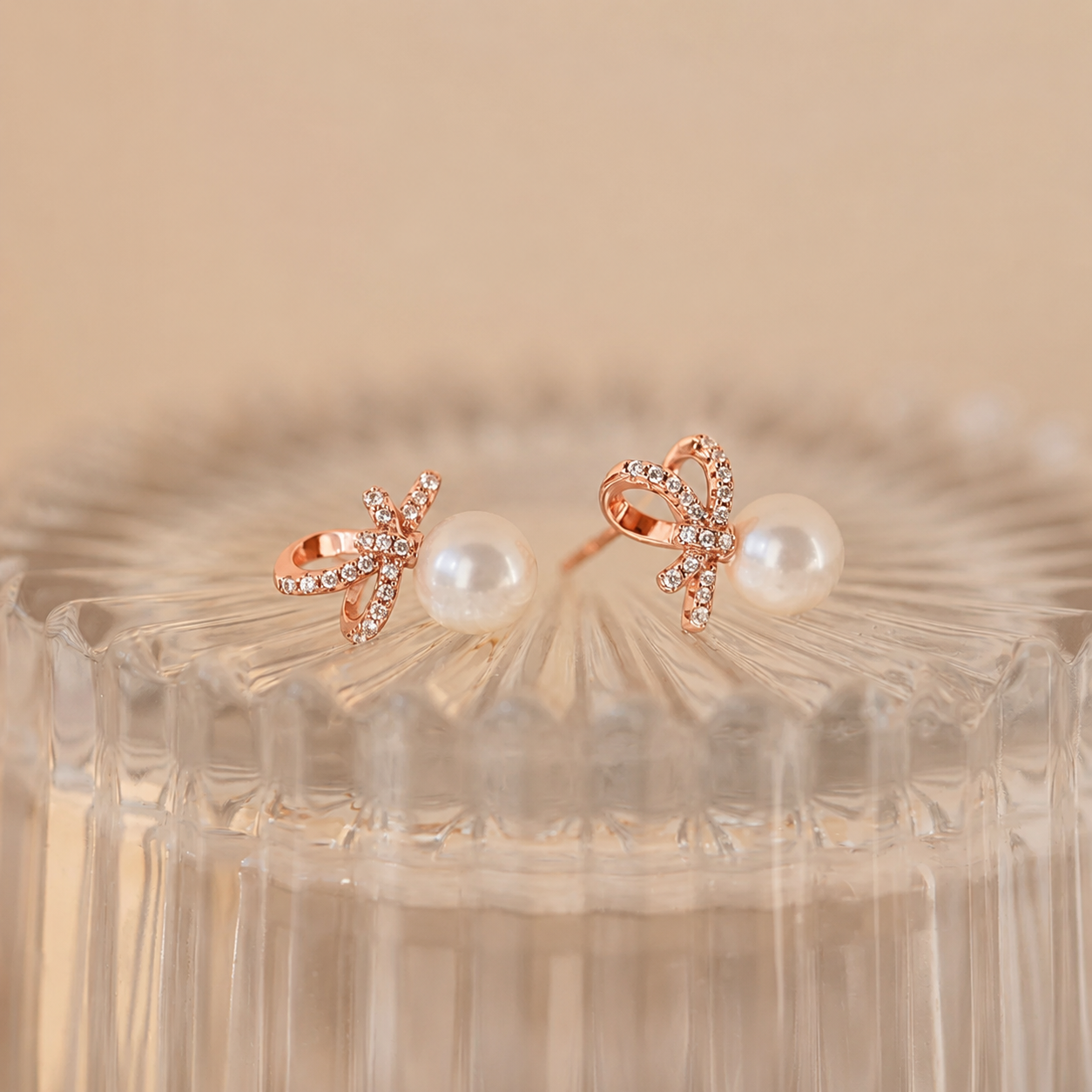 Rose gold earrings with pearl centers on a textured beige background