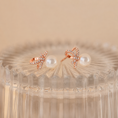 Rose gold earrings with pearl centers on a textured beige background