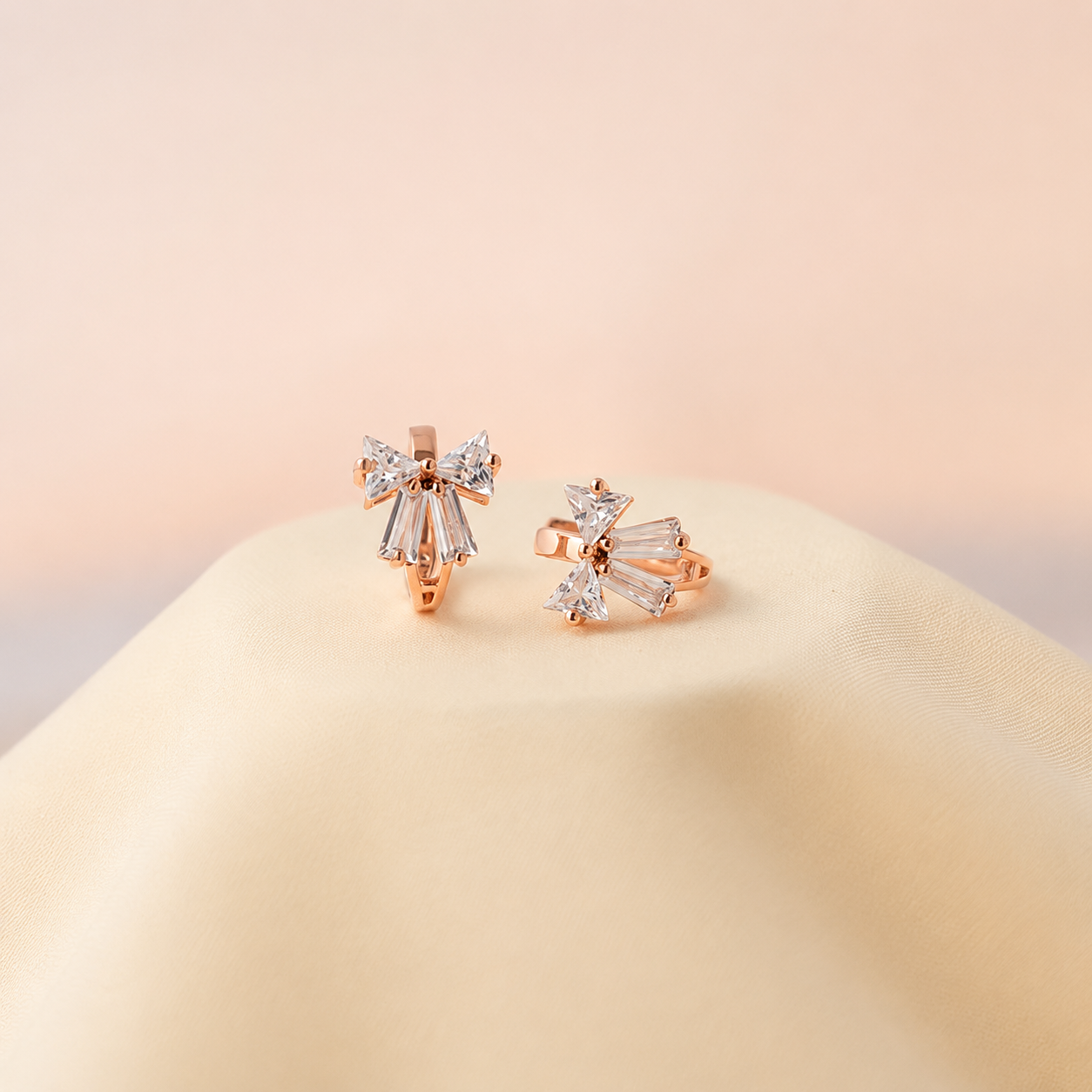Rose gold earrings with clear gemstones on a beige surface