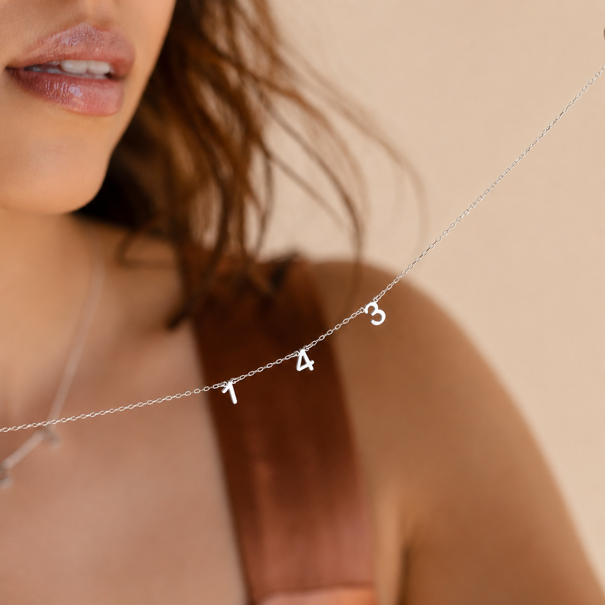 Close-up of a woman wearing a silver necklace with numbers on a beige background