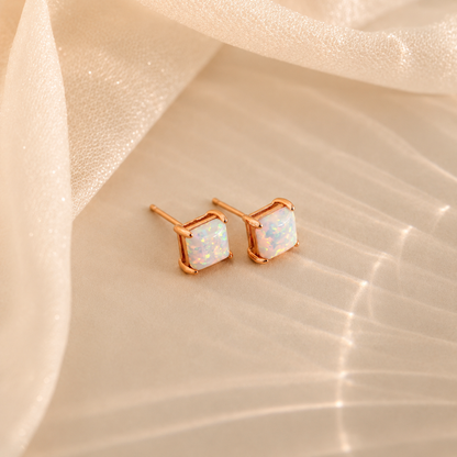 Rose gold earrings with white gemstones on a beige fabric background