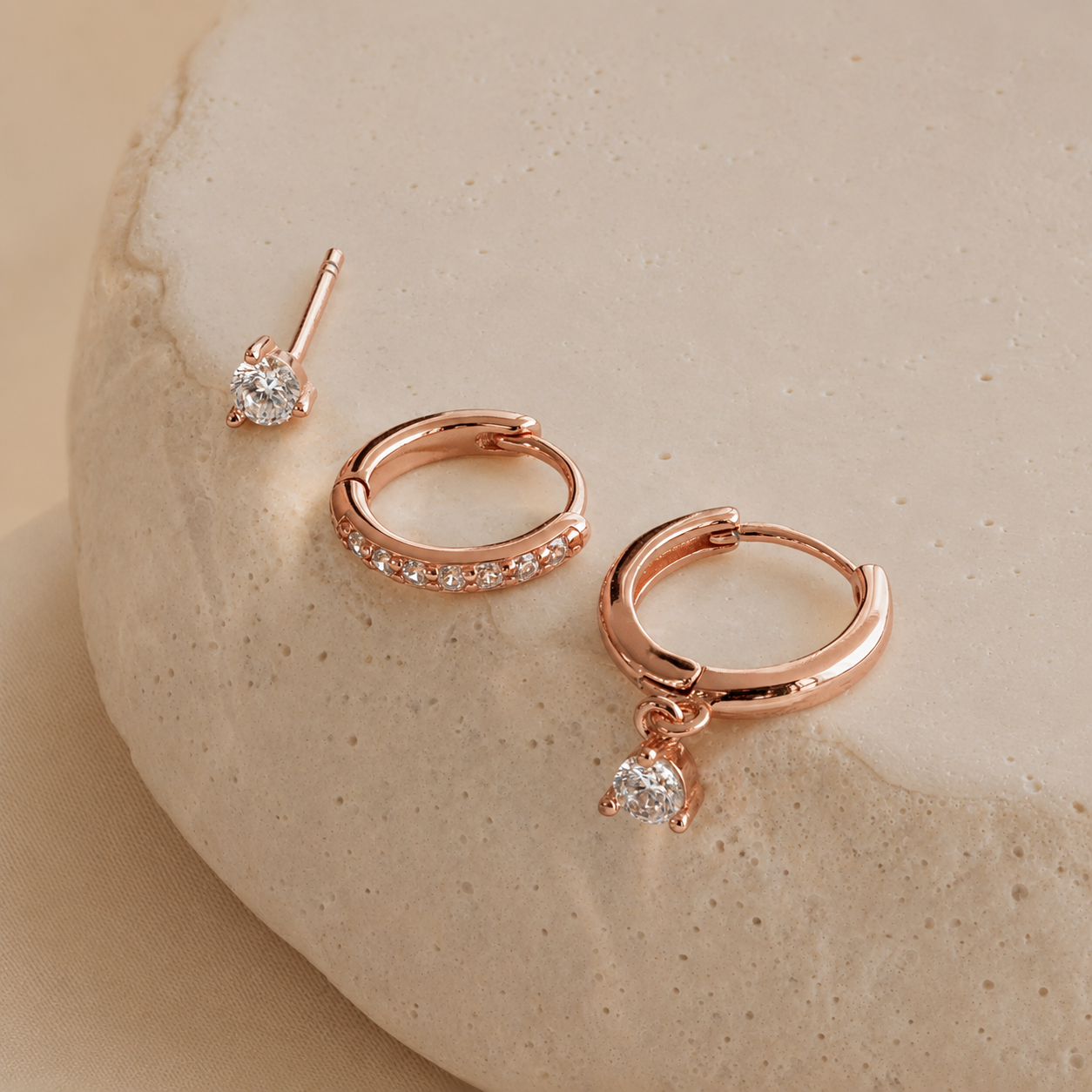 Rose gold hoop earrings with small diamonds on a beige stone background