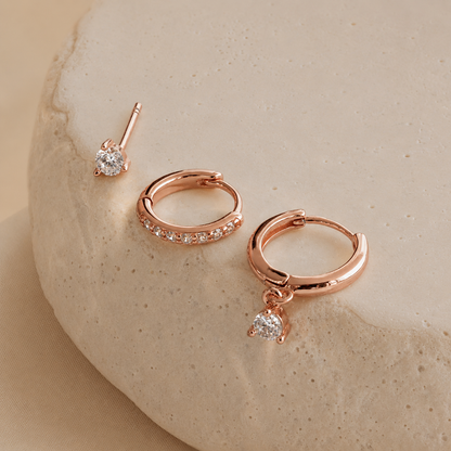 Rose gold hoop earrings with small diamonds on a beige stone background