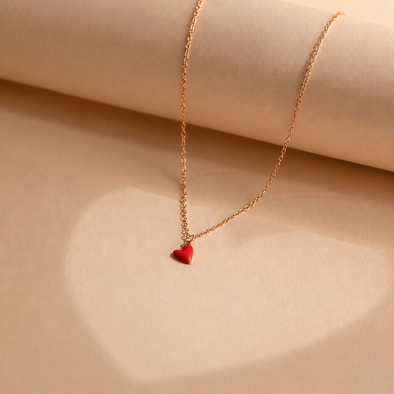 Gold necklace with a red heart pendant on a beige background