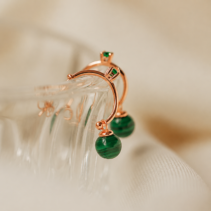 Rose gold earrings with green gemstones on a soft beige background