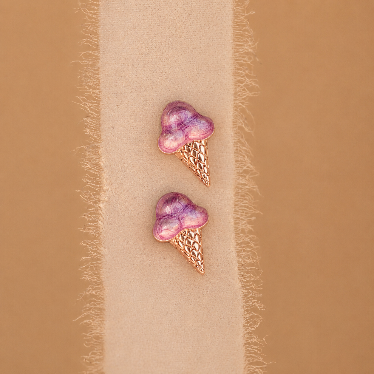 Purple ice cream cone earrings on a beige fabric background