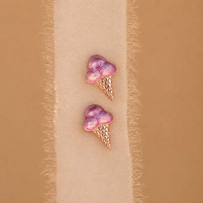 Purple ice cream cone earrings on a beige fabric background