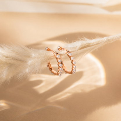 Pair of rose gold hoop earrings with pearls on a beige background