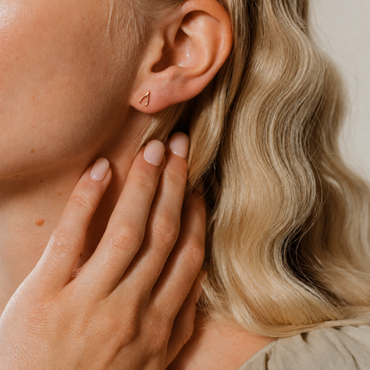 Close-up of a person wearing a gold earring with a hand touching the ear.