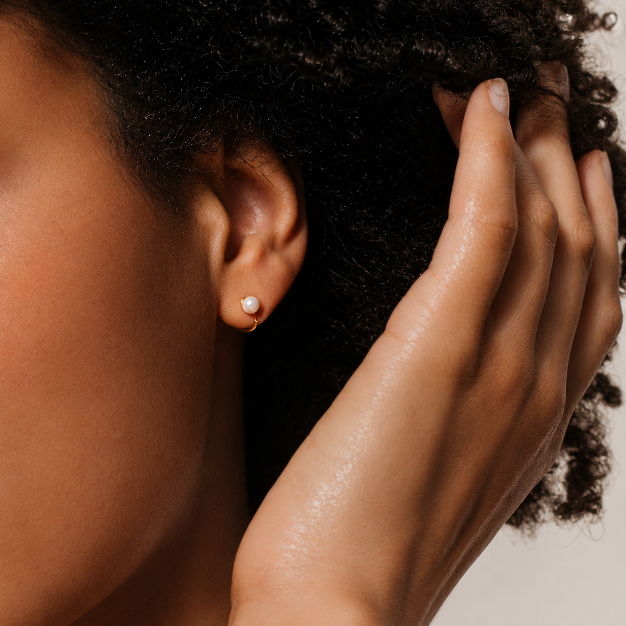 Close-up of a person's ear with an earring and hand touching hair.