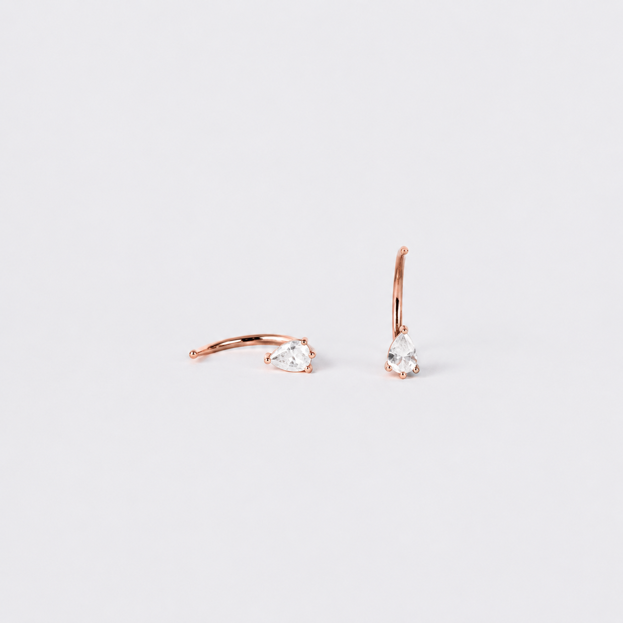 Rose gold hoop earrings with clear gemstones on a light gray background
