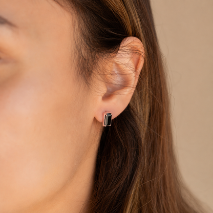 Close-up of an ear wearing a green gemstone earring against a neutral background