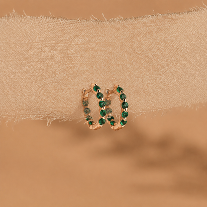 Gold hoop earrings with green gemstones on a beige fabric background
