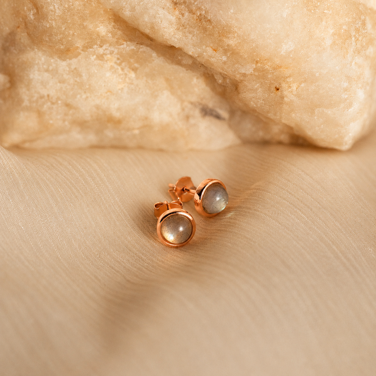 Rose gold earrings with gemstones on a beige fabric background