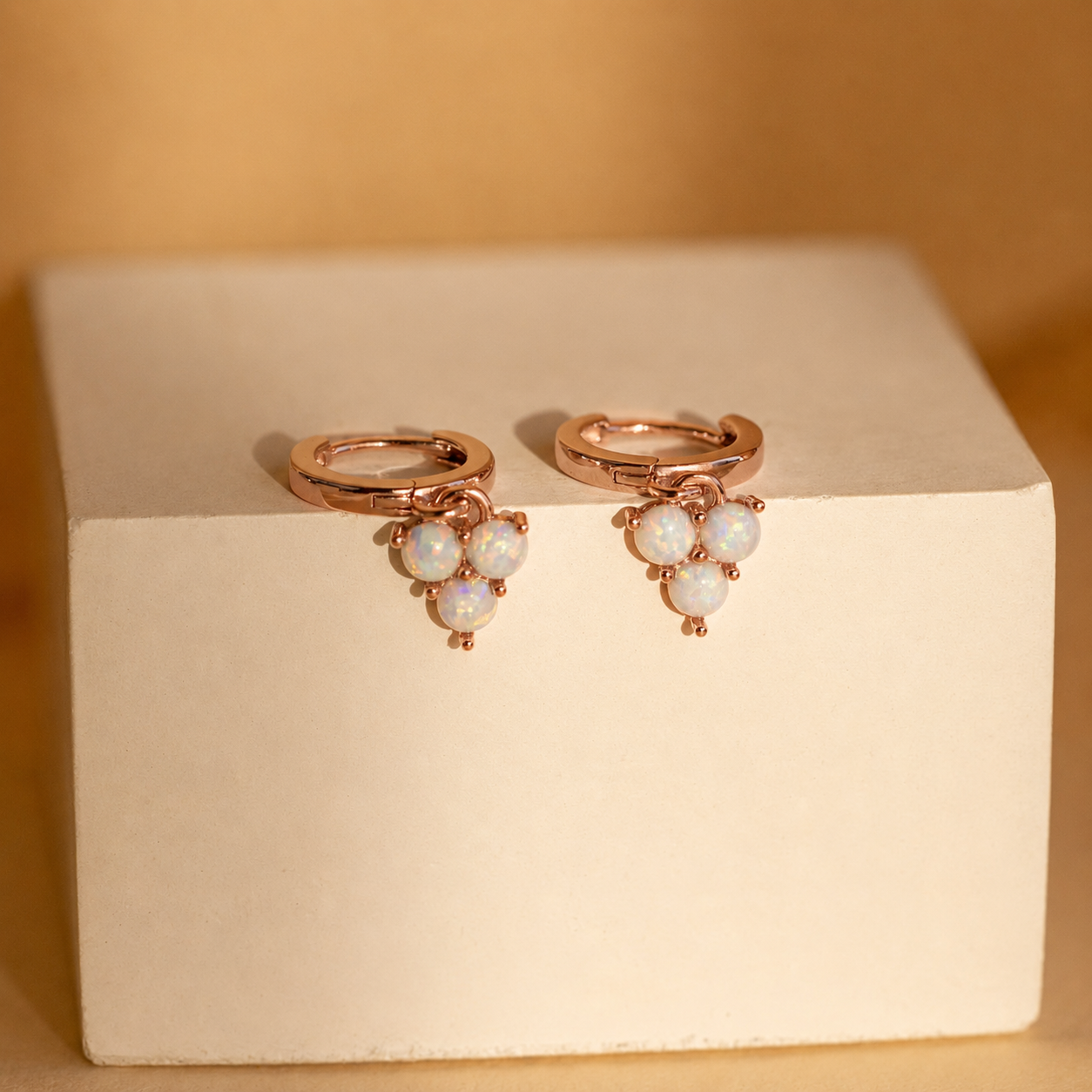 Rose gold earrings with pearl-like stones on a beige box against a beige background