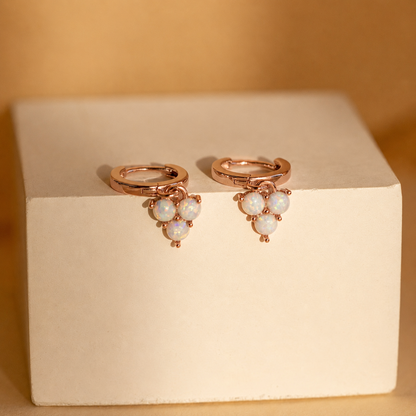 Rose gold earrings with pearl-like stones on a beige box against a beige background