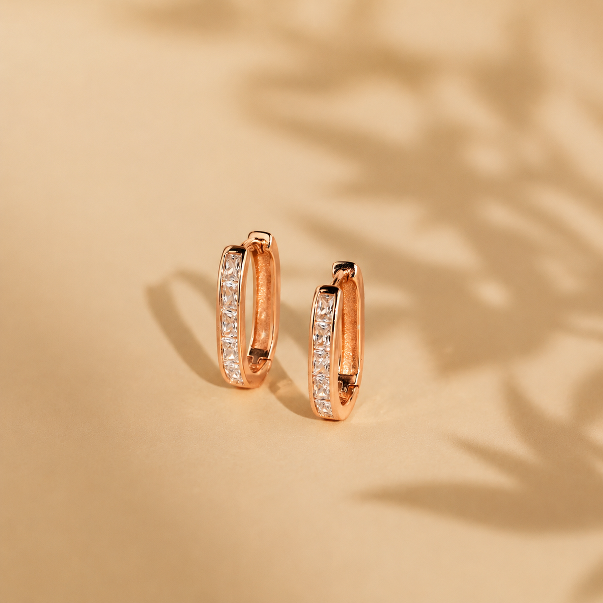 Rose gold hoop earrings with embedded diamonds on a beige background