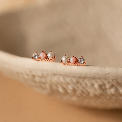 Pair of rose gold earrings with pearls and gemstones on a beige surface