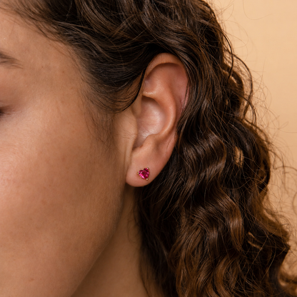 Close-up of an ear wearing a pink gemstone earring with wavy hair.