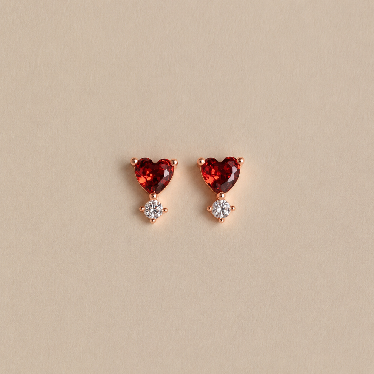 Heart-shaped red gemstone earrings with rose gold setting on a beige background